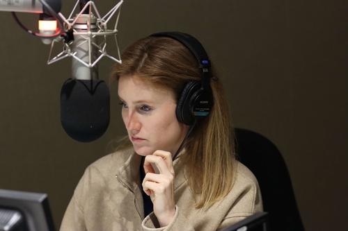Carolyn Beeler, a redheaded woman wearing headphones, speaks into a recording studio microphone