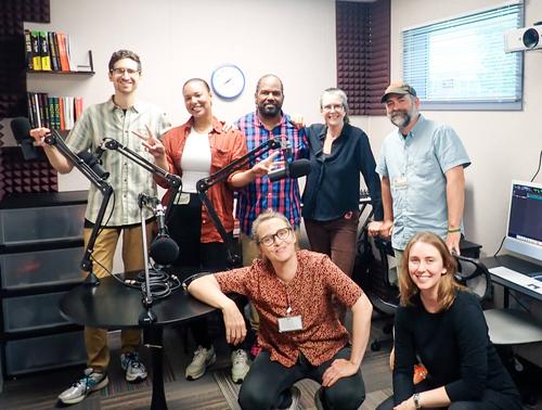 A diverse group of people pose for a picture in an audio studio
